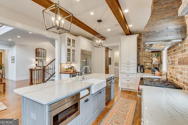 kitchen with built in appliances, brick wall, light wood-style floors, white cabinets, and a sink