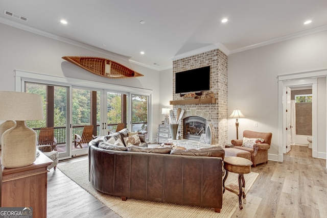 living area featuring a brick fireplace, visible vents, ornamental molding, and light wood-style flooring