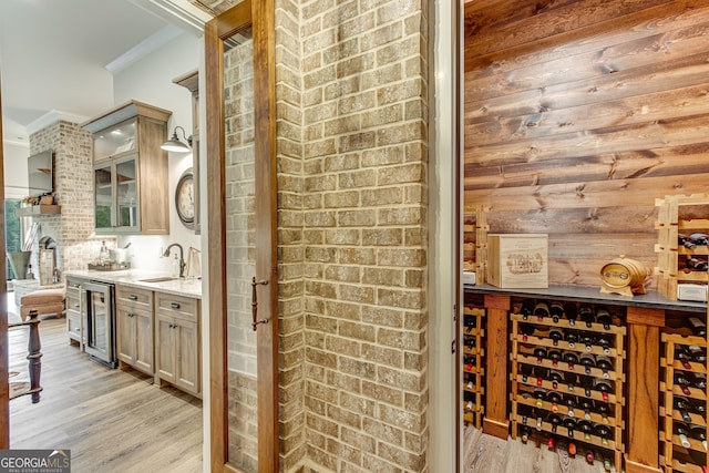 wine cellar with ornamental molding, wine cooler, indoor wet bar, a sink, and light wood-style flooring