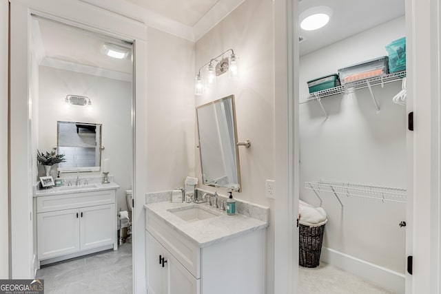 bathroom with a walk in closet, two vanities, and a sink