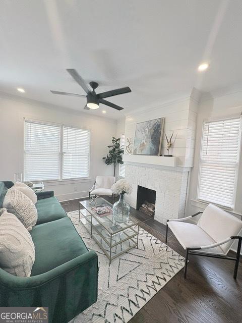 living area featuring wood finished floors, a ceiling fan, ornamental molding, a brick fireplace, and recessed lighting