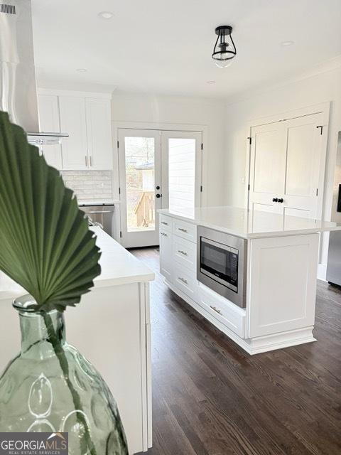 kitchen with stainless steel microwave, white cabinetry, dark wood-style flooring, and light countertops