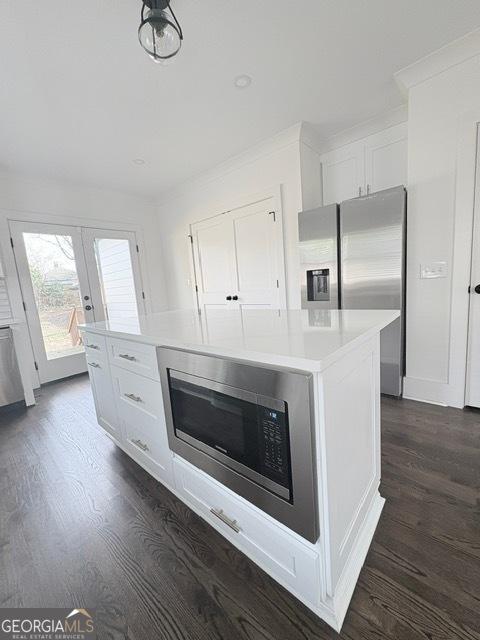 kitchen featuring dark wood-style flooring, stainless steel appliances, white cabinets, light countertops, and a kitchen island