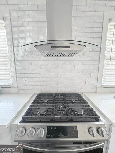 kitchen view of range hood, decorative backsplash, stainless steel gas range oven, and light countertops