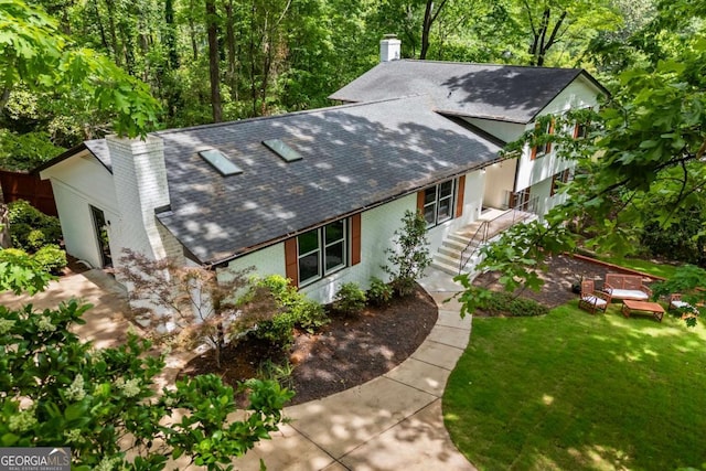 view of front of home with a shingled roof, a front yard, and a chimney
