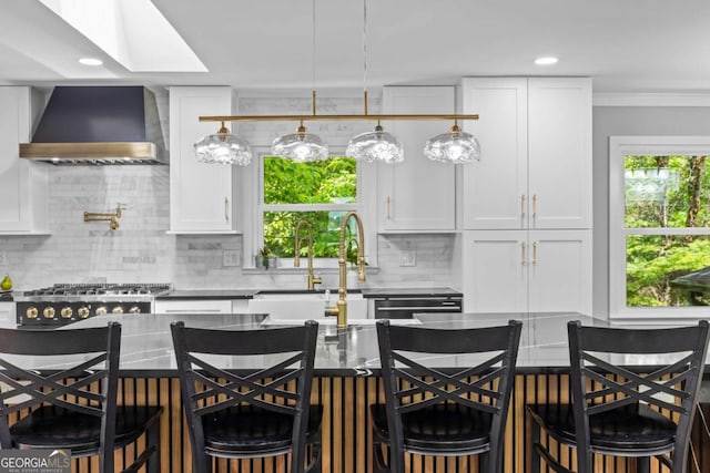 kitchen featuring wall chimney range hood, white cabinetry, a skylight, and backsplash