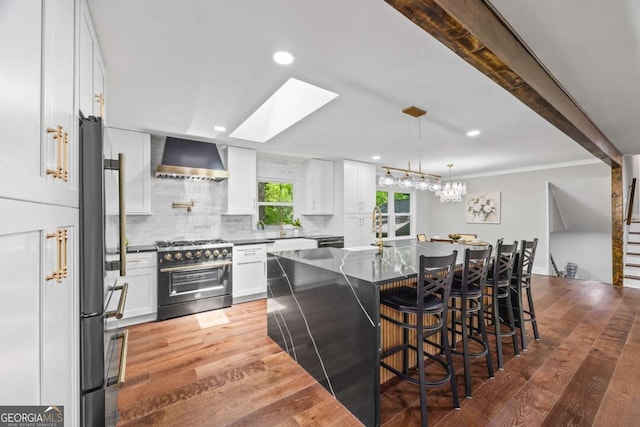 kitchen featuring white cabinets, wall chimney exhaust hood, stainless steel appliances, backsplash, and a skylight
