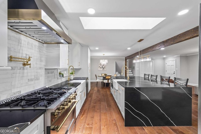 kitchen with dark countertops, high end range, a skylight, and wall chimney range hood