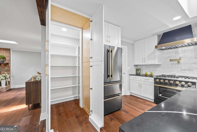 kitchen with wall chimney range hood, premium appliances, dark wood-style floors, and white cabinets
