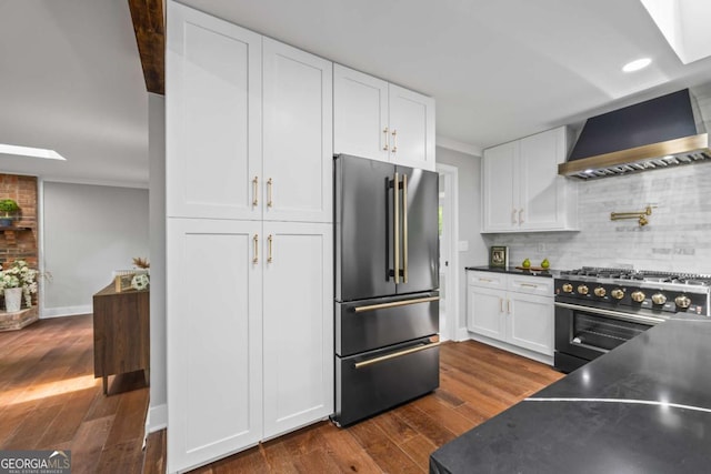 kitchen featuring wall chimney range hood, dark wood-style flooring, white cabinetry, high end appliances, and tasteful backsplash