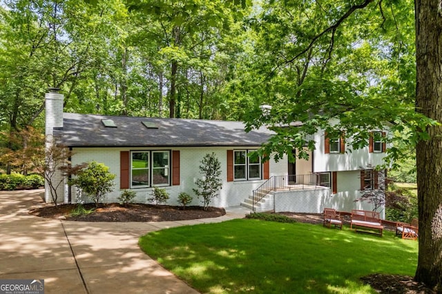split level home with a shingled roof, a chimney, a front yard, and brick siding