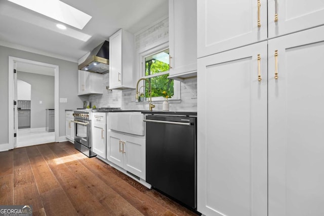 kitchen with wall chimney range hood, a skylight, tasteful backsplash, white cabinets, and black dishwasher