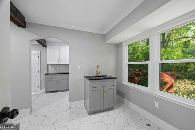 interior space featuring a sink, arched walkways, crown molding, and dark countertops