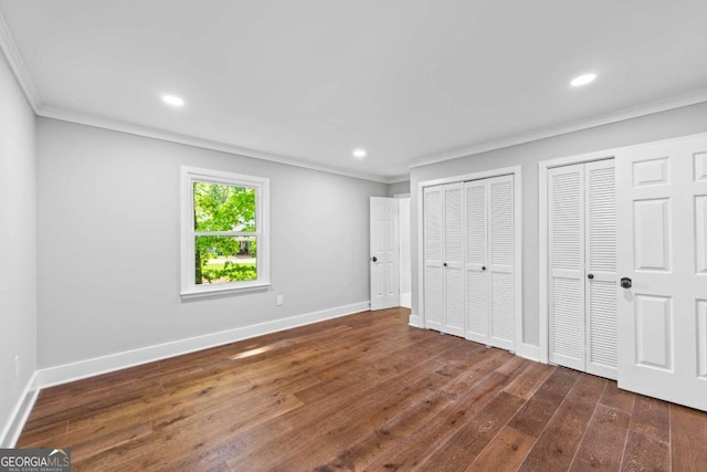 unfurnished bedroom with dark wood-style flooring, multiple closets, recessed lighting, baseboards, and ornamental molding