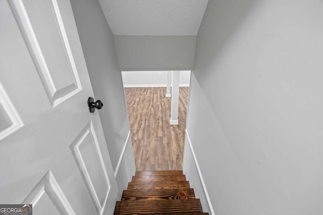 stairs featuring baseboards, a textured ceiling, and wood finished floors