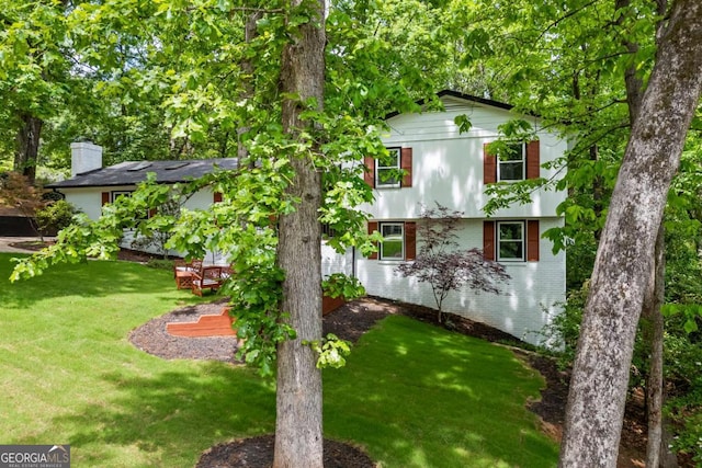 rear view of property featuring a lawn, a chimney, and brick siding