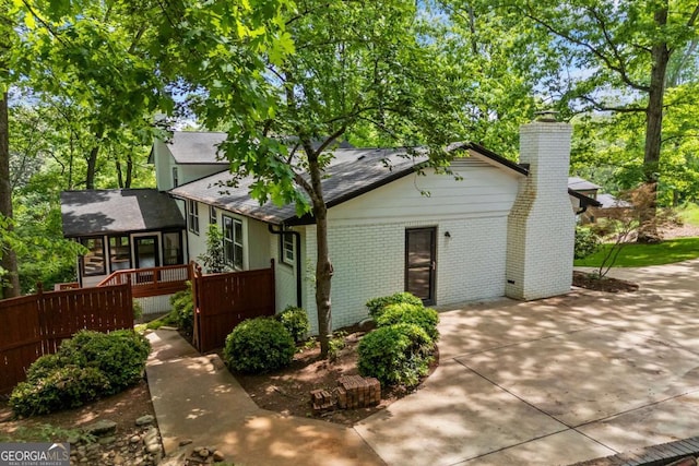 view of front of house with a chimney, a sunroom, brick siding, a patio, and a shingled roof