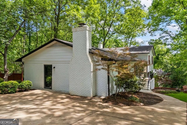 view of side of property with brick siding, a patio area, and a chimney
