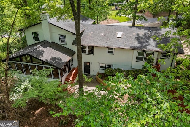 back of house with a shingled roof, a sunroom, and a chimney