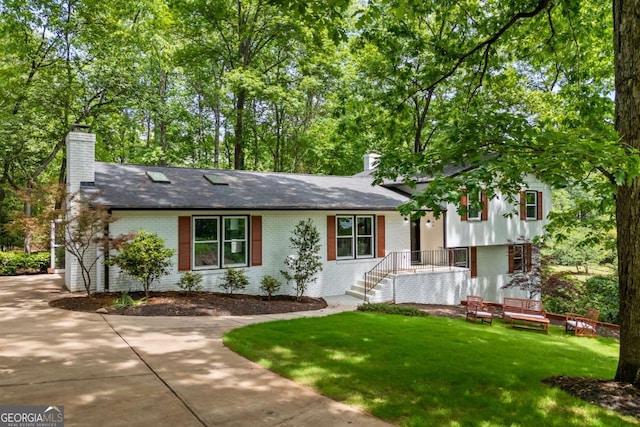 split level home with brick siding, a chimney, and a front yard