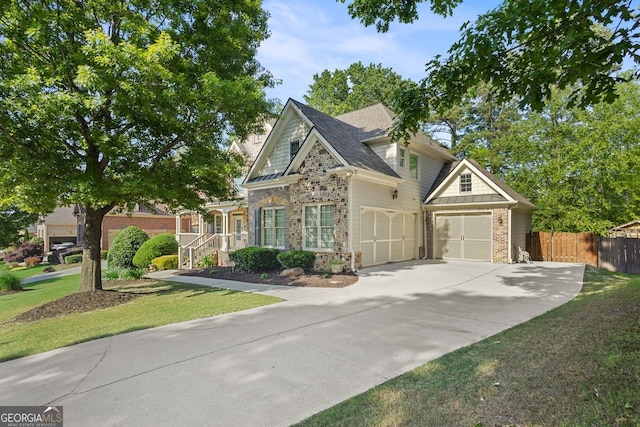 craftsman house with fence, a front yard, driveway, and stone siding