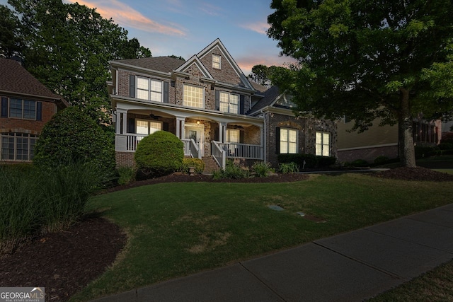 craftsman house with covered porch, brick siding, and a yard