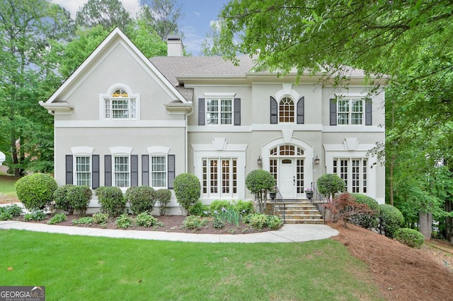 view of front facade with a front lawn, stucco siding, french doors, and a chimney