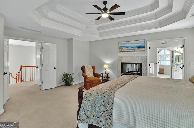 bedroom featuring a high end fireplace, baseboards, ornamental molding, light carpet, and a tray ceiling