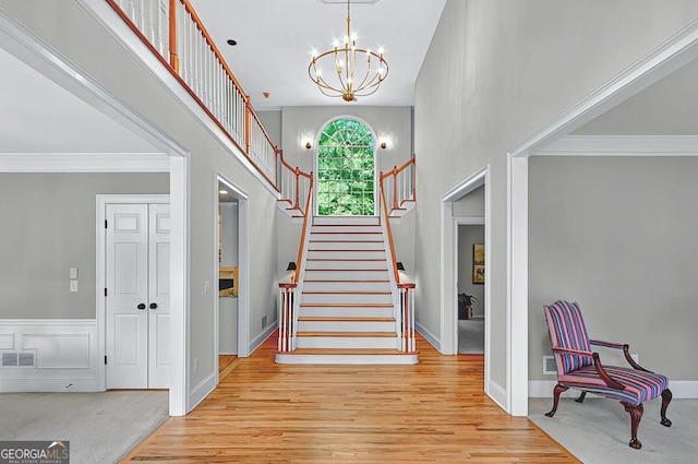 entrance foyer featuring an inviting chandelier, light wood finished floors, visible vents, ornamental molding, and stairway