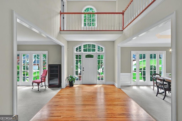 foyer entrance with french doors, baseboards, wood finished floors, a towering ceiling, and ornamental molding