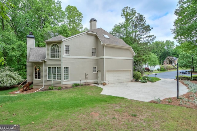 rear view of property with a chimney, a lawn, concrete driveway, an attached garage, and a shingled roof