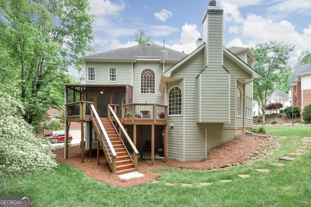 back of property featuring a chimney, a deck, a sunroom, stairway, and a yard