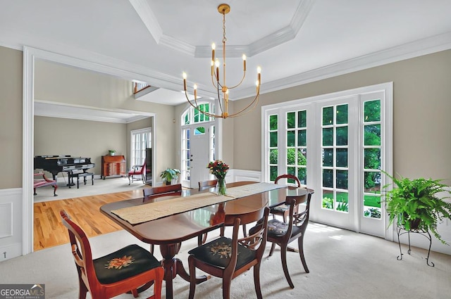 dining space featuring crown molding, wainscoting, wood finished floors, an inviting chandelier, and a tray ceiling