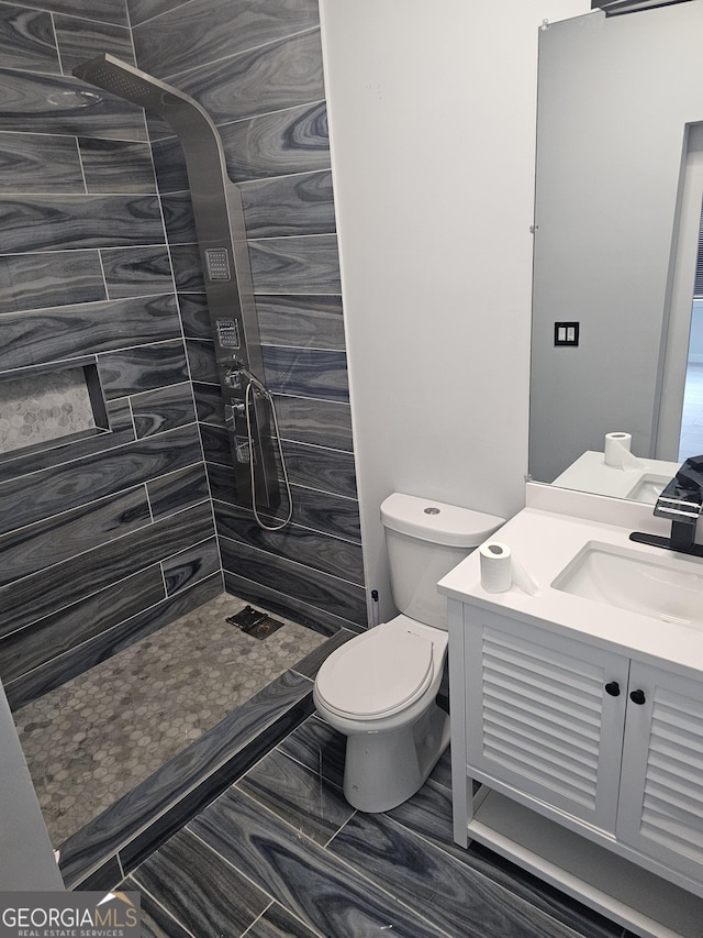 bathroom featuring vanity, a tile shower, and toilet