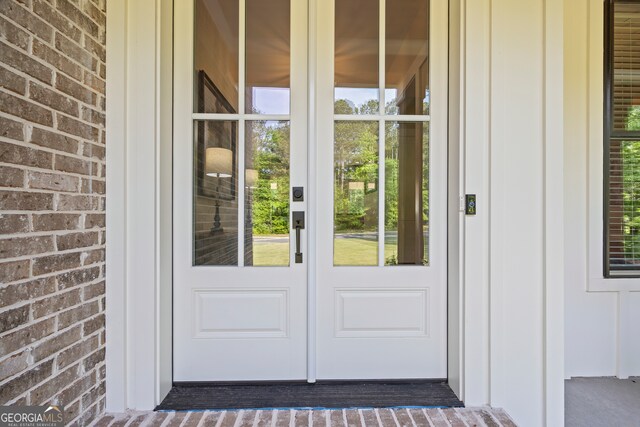 view of exterior entry with french doors, board and batten siding, and brick siding