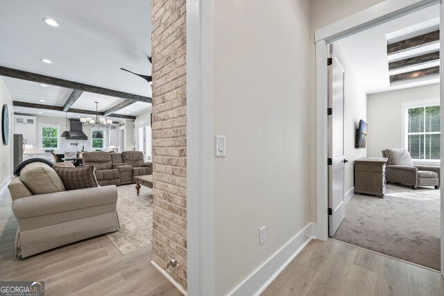 hall featuring light wood-style flooring, beam ceiling, a chandelier, and a healthy amount of sunlight