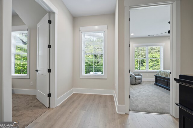 doorway with baseboards, light colored carpet, and light wood-style floors