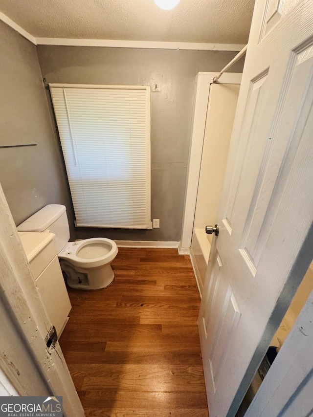 bathroom with a textured ceiling, wood finished floors, toilet,  shower combination, and ornamental molding