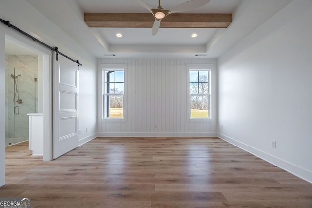 spare room featuring a healthy amount of sunlight, baseboards, a barn door, and wood finished floors