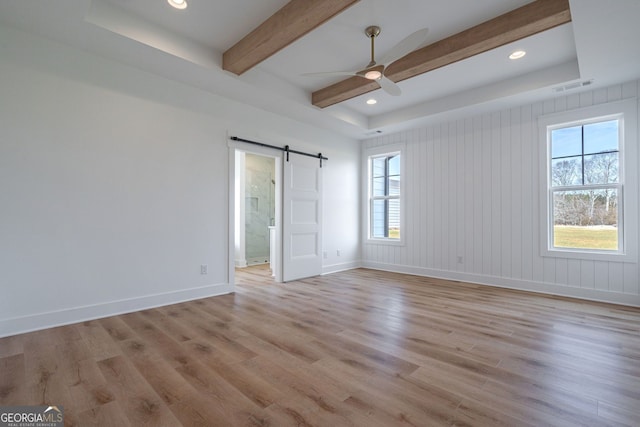 unfurnished room with light wood-style floors, a barn door, a ceiling fan, and a healthy amount of sunlight
