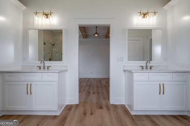 full bath with a stall shower, wood finished floors, two vanities, a sink, and baseboards