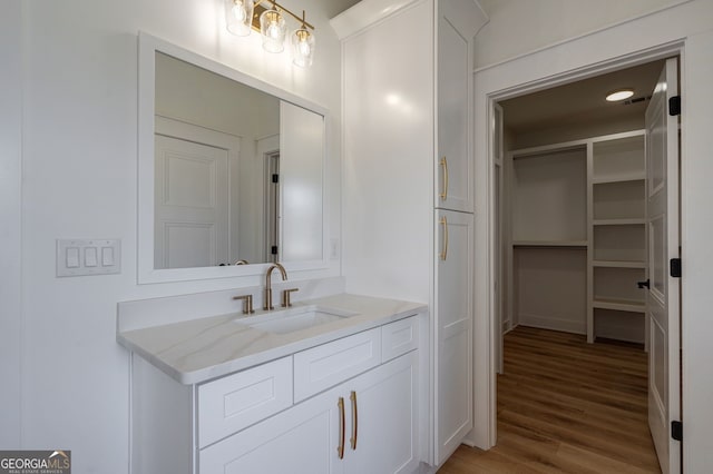 bathroom with a walk in closet, wood finished floors, and vanity