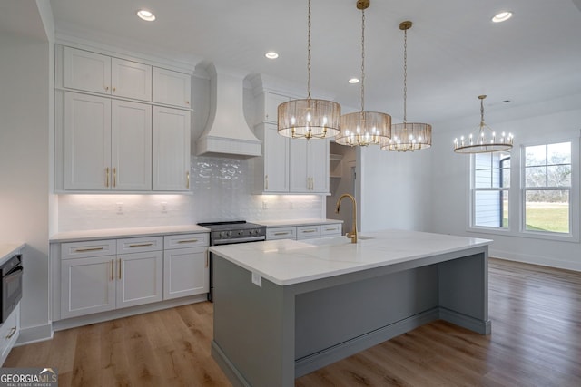 kitchen featuring an inviting chandelier, tasteful backsplash, a sink, custom range hood, and light wood-type flooring