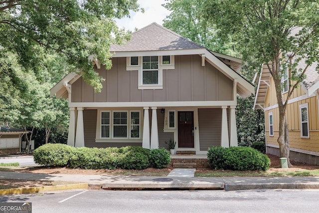view of front of home with board and batten siding, roof with shingles, uncovered parking, and a porch