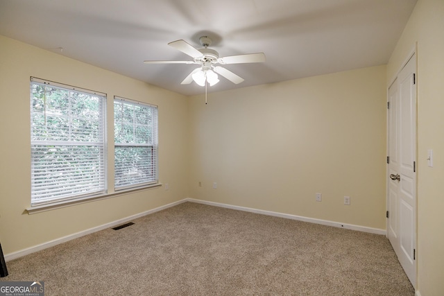 carpeted spare room with visible vents, baseboards, and ceiling fan