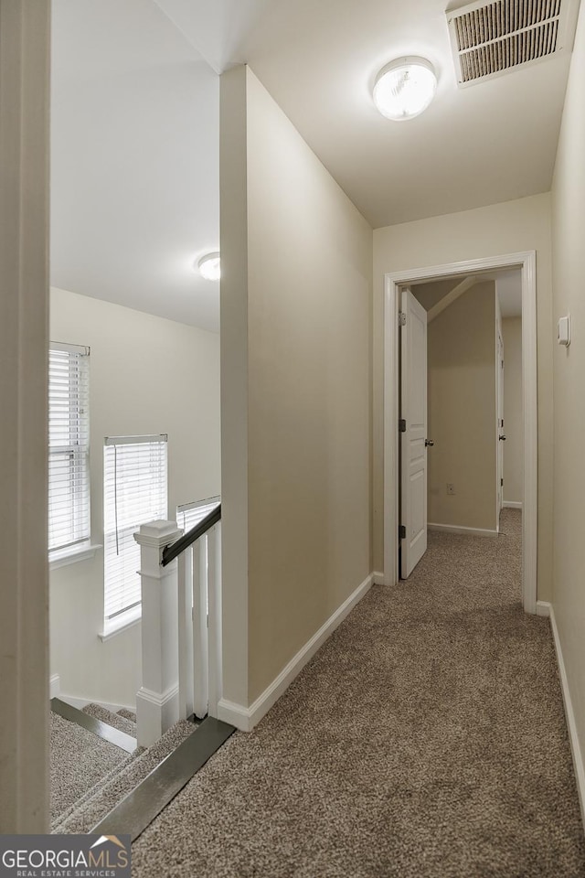 hall with visible vents, carpet flooring, baseboards, and an upstairs landing