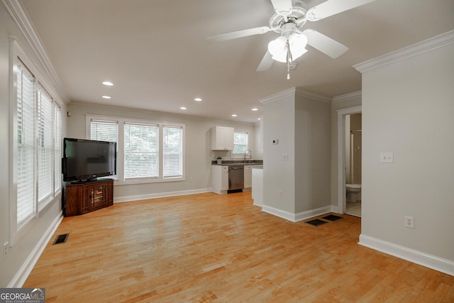 unfurnished living room featuring a sink, ornamental molding, light wood finished floors, and visible vents