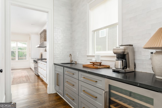 bar with dark wood-style flooring, tasteful backsplash, a sink, high end stainless steel range, and wine cooler