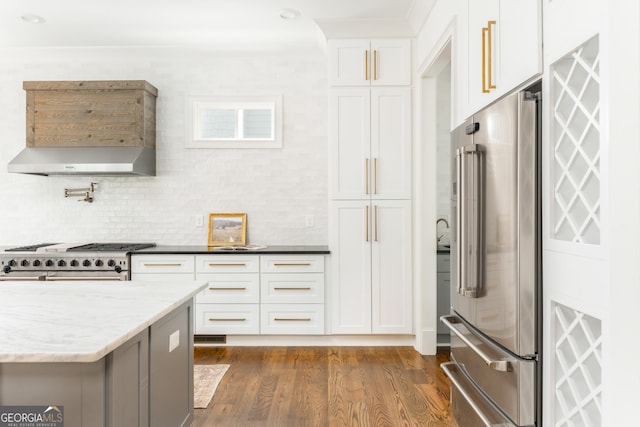 kitchen with wall chimney range hood, high quality appliances, light stone counters, dark wood-style floors, and white cabinetry