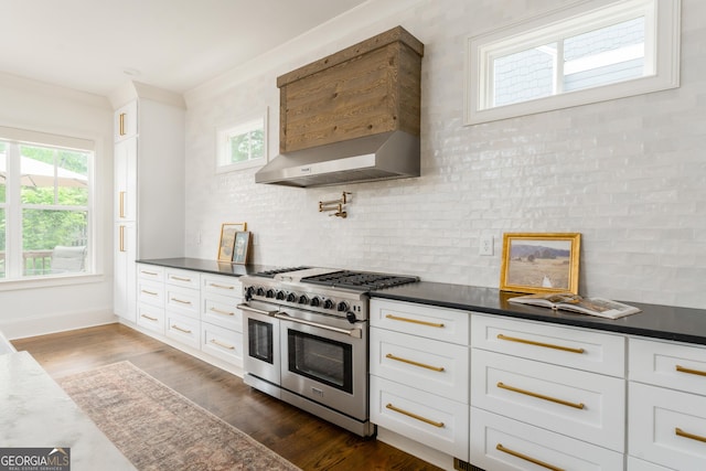 kitchen featuring dark countertops, wall chimney range hood, white cabinetry, range with two ovens, and backsplash